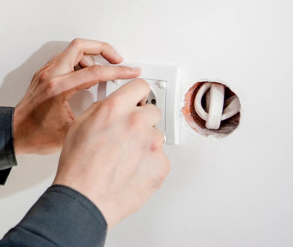 Las manos de un electricista colocando un enchufe en una pared blanca